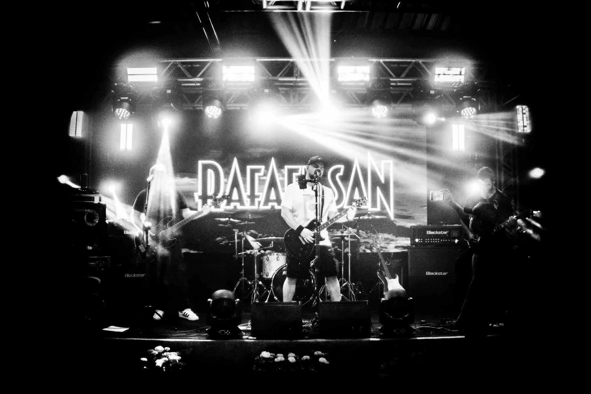 Rafael San no palco com iluminação e identidade visual ao fundo